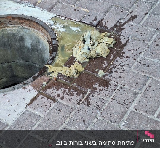 פתח ביוב עם פסולת על המדרכה